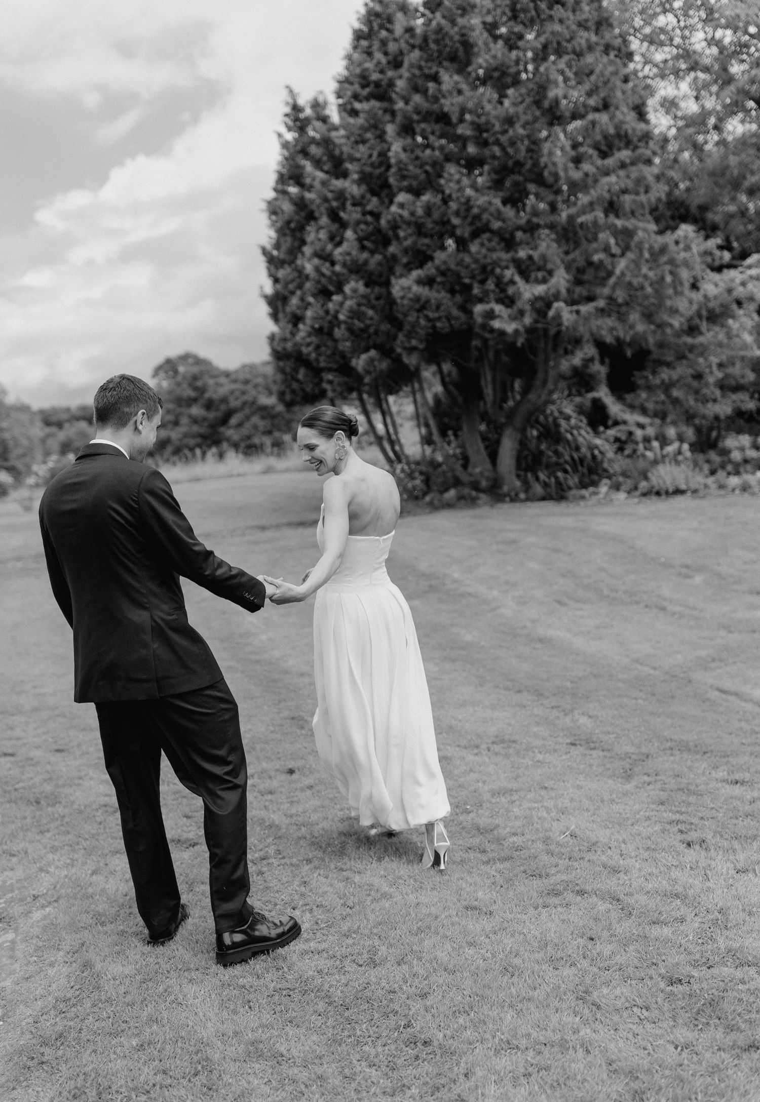 A couple walking hand in hand across a grassy field on their wedding day.