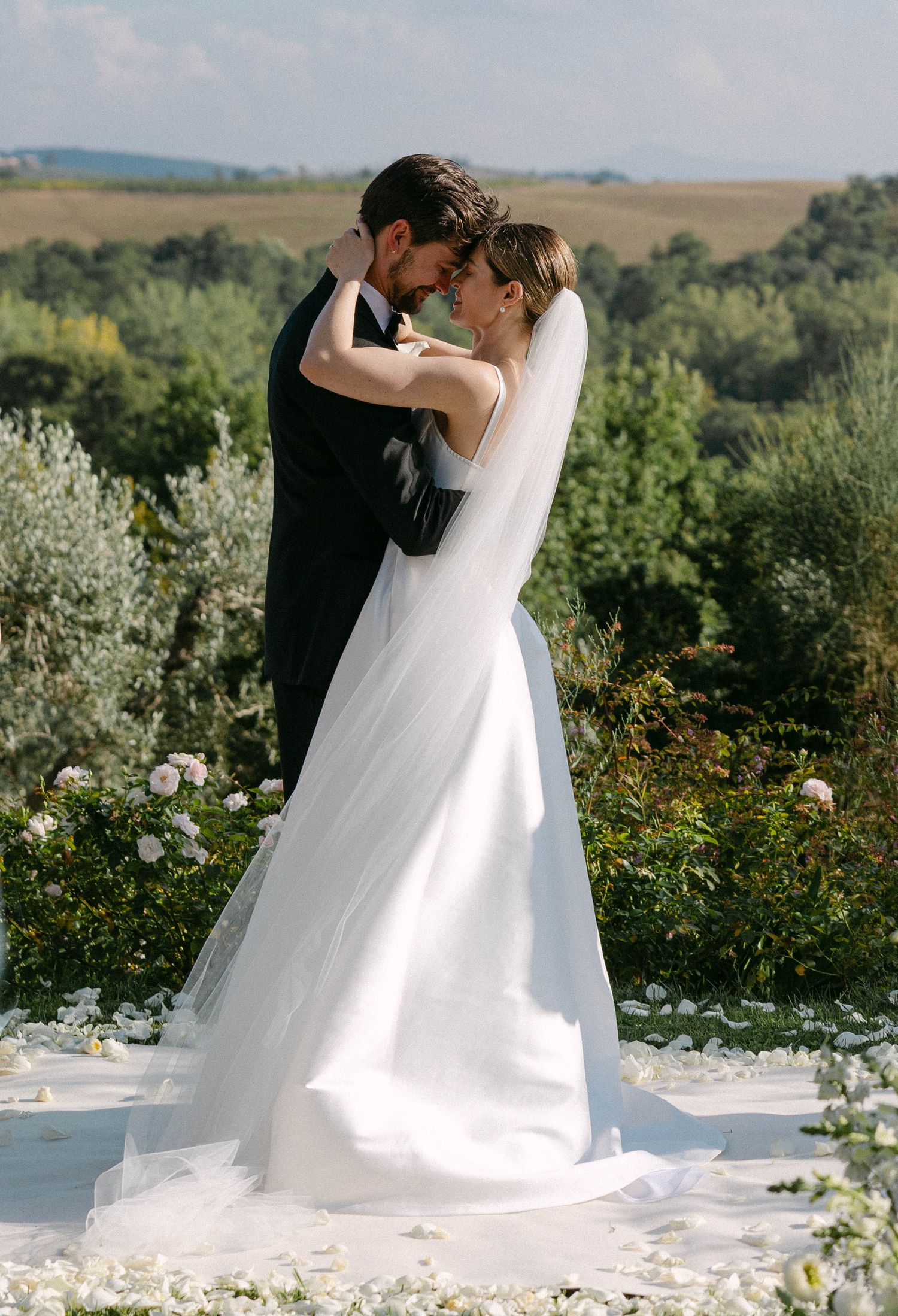 A romantic outdoor wedding ceremony with white flower petals scattered along the ground. Tuscany Wedding.
