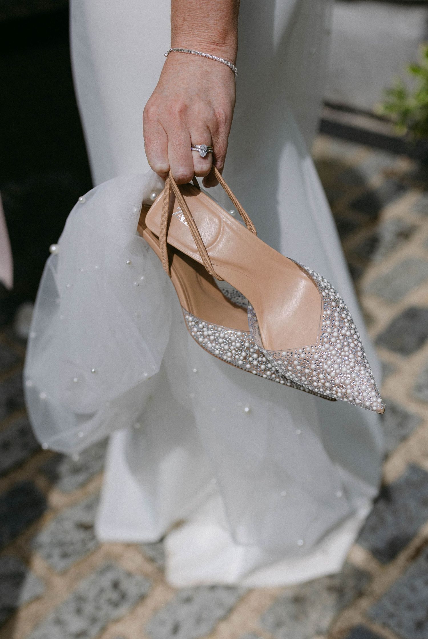 Close-up of sparkly bridal shoes with crystal embellishments against white dress fabric.