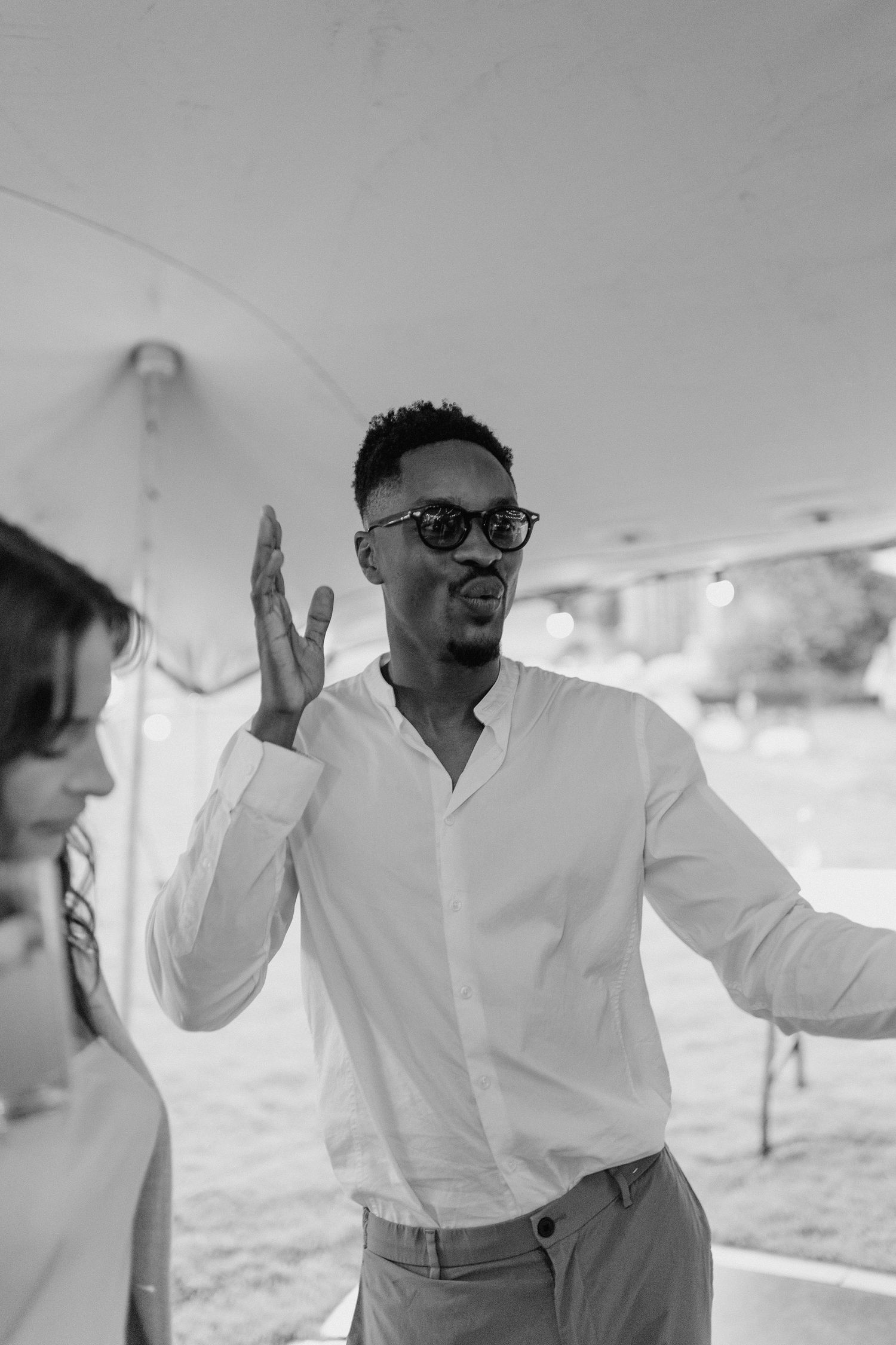 Person in white shirt and glasses dancing joyfully under a tent.