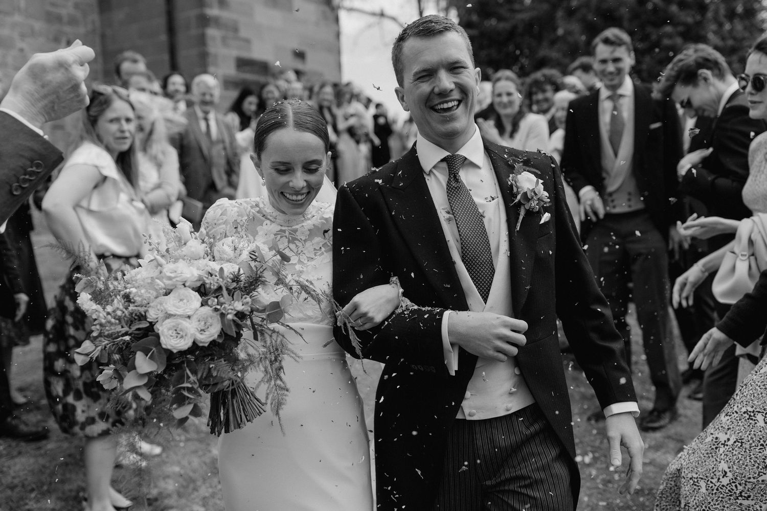 Wedding guests throw confetti and celebrate during an outdoor ceremony.