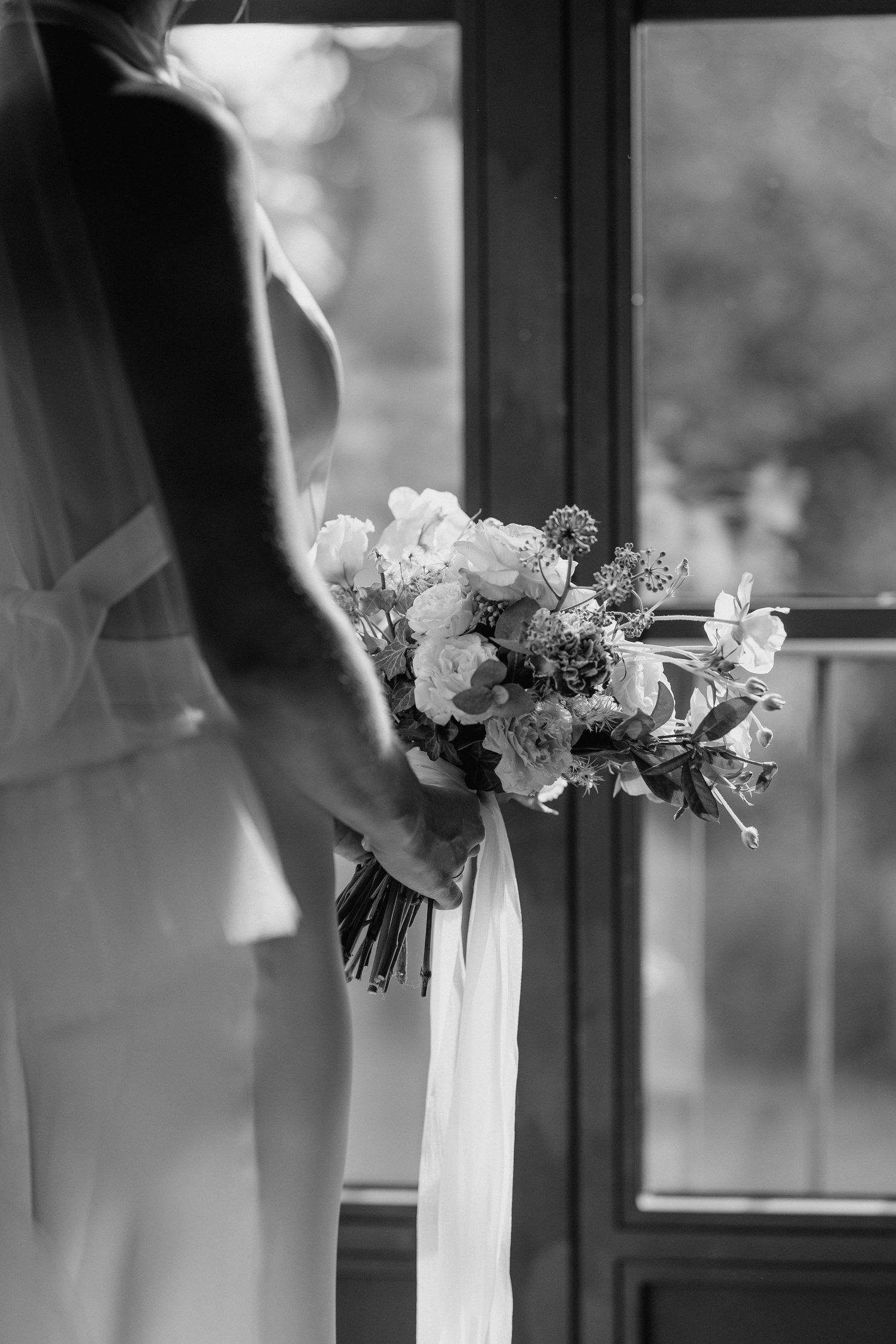 Elegant white floral bouquet with flowing ribbons captured in window light.