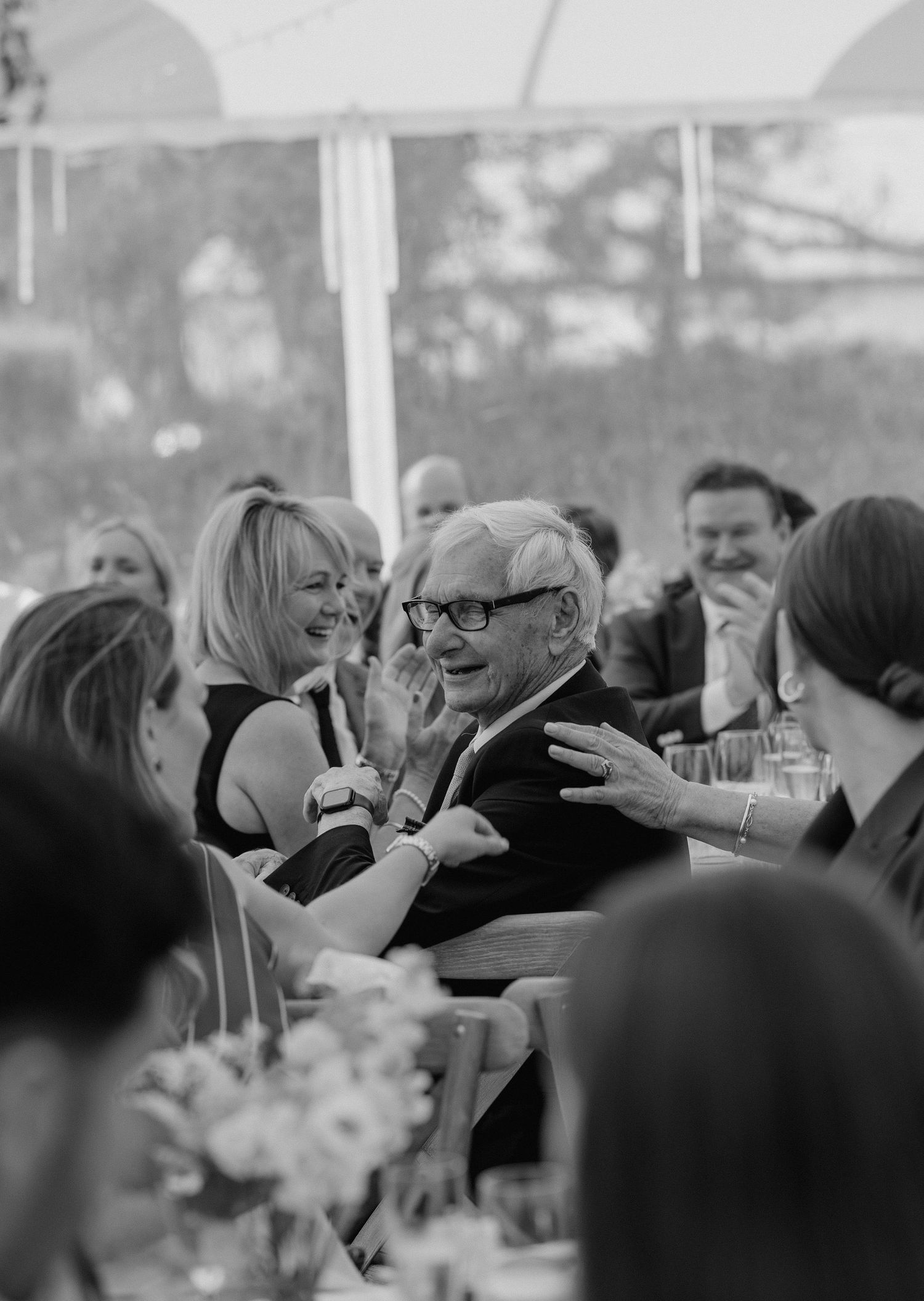 Candid black and white photo of wedding guests laughing during reception.