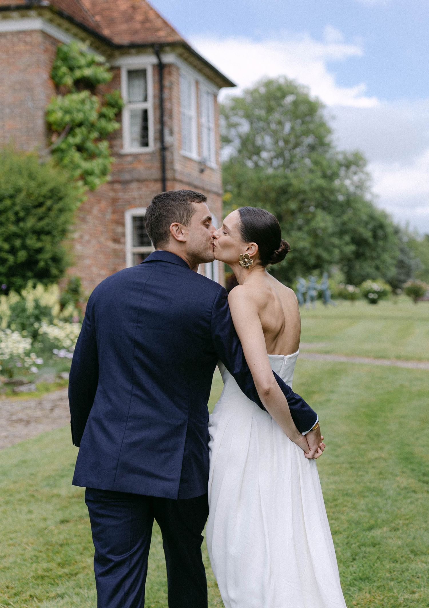 A couple shares intimate kisses on a grassy lawn outside a brick building on their wedding day.