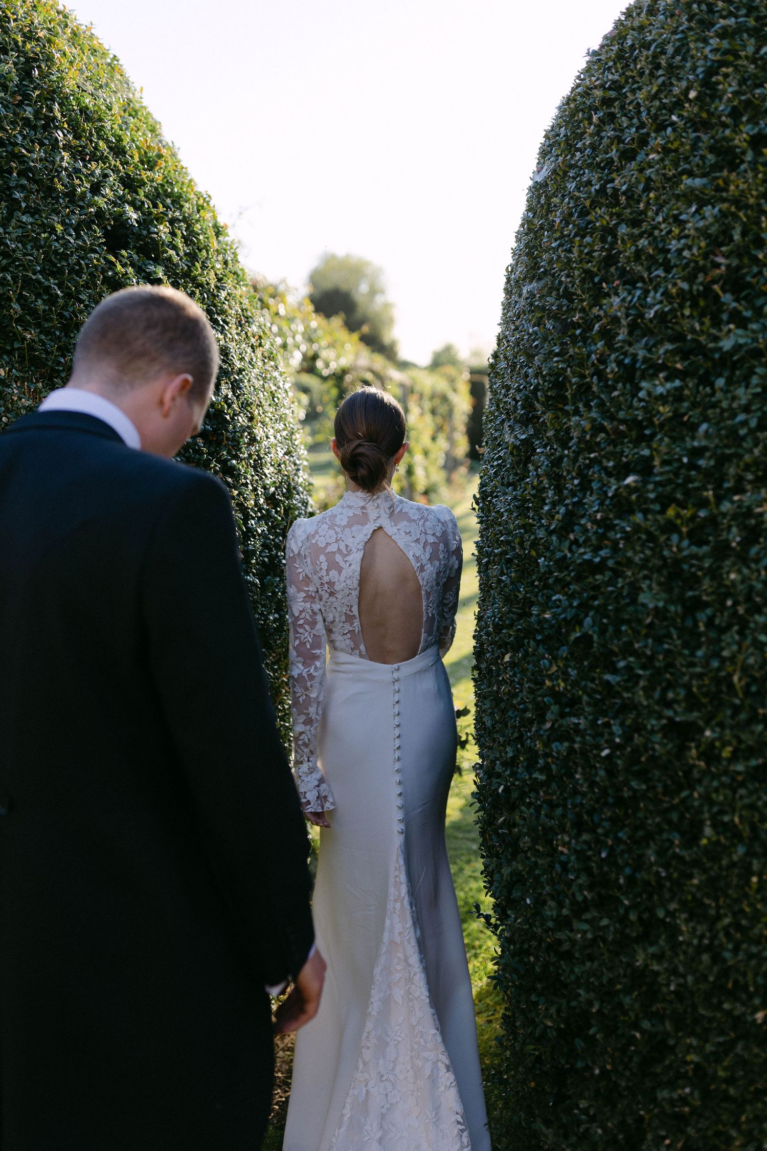 A couple walking through a manicured garden path between tall hedges.