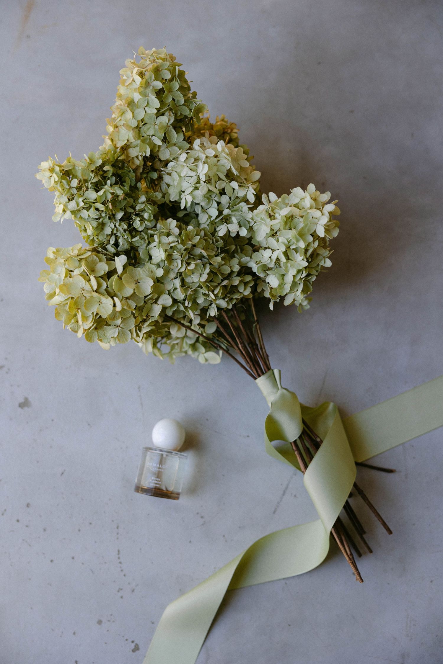Cream-colored hydrangea bouquet being wrapped with a pale mint green ribbon.