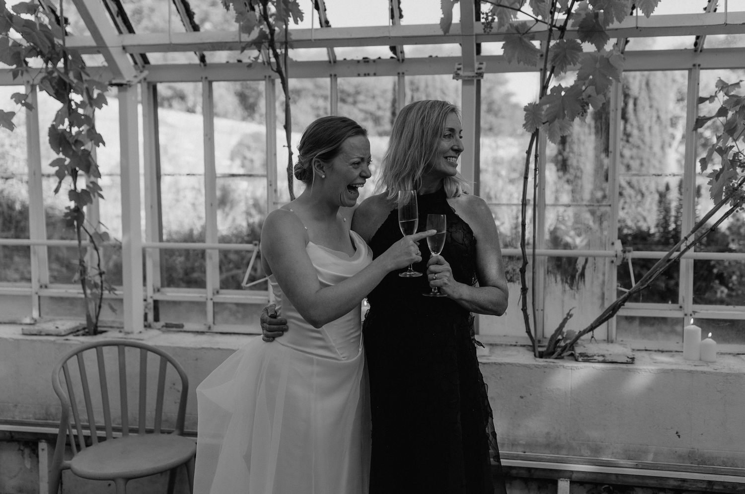 Wedding celebration in greenhouse with guests sharing drinks and conversation.