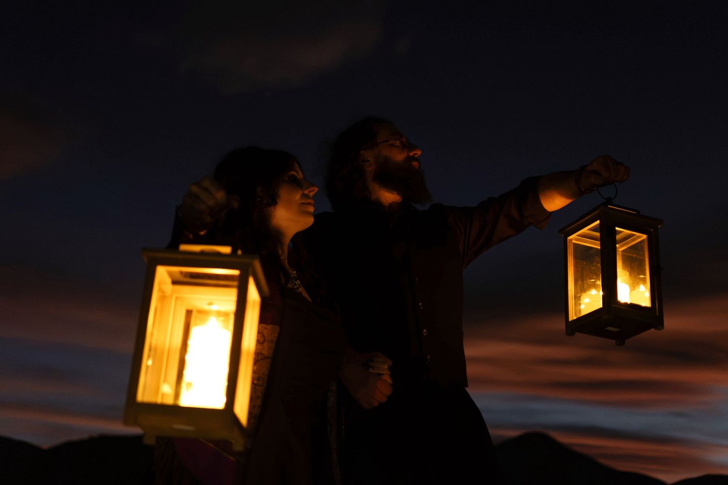 Couple holding glowing lanterns against a dramatic night sky at dusk elopement.