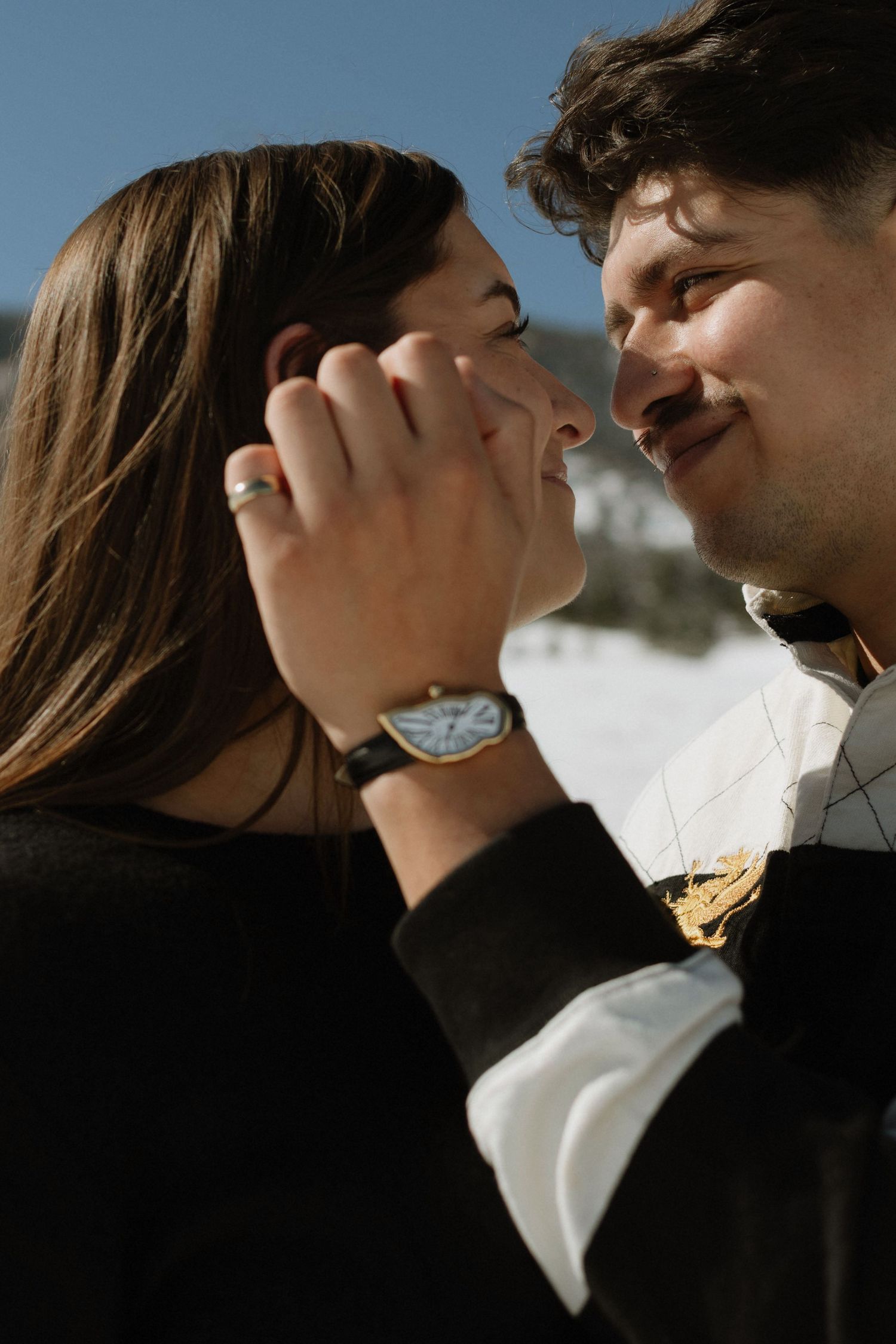 Romantic couple sharing a tender moment outdoors in winter, man wearing a classic watch, woman with an engagement ring.