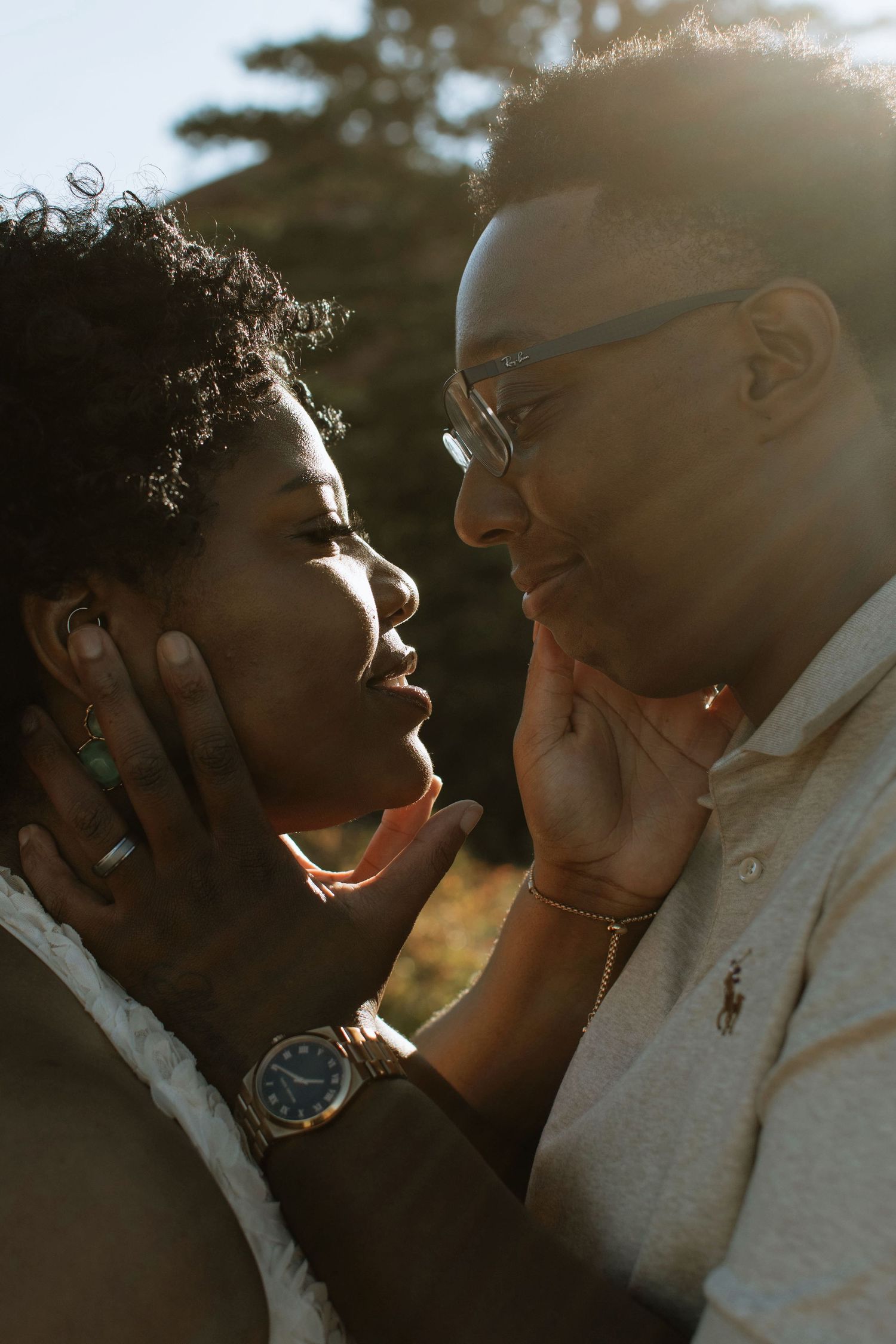 A couple shares a tender moment face-to-face in golden backlight, touching each other's faces with love.