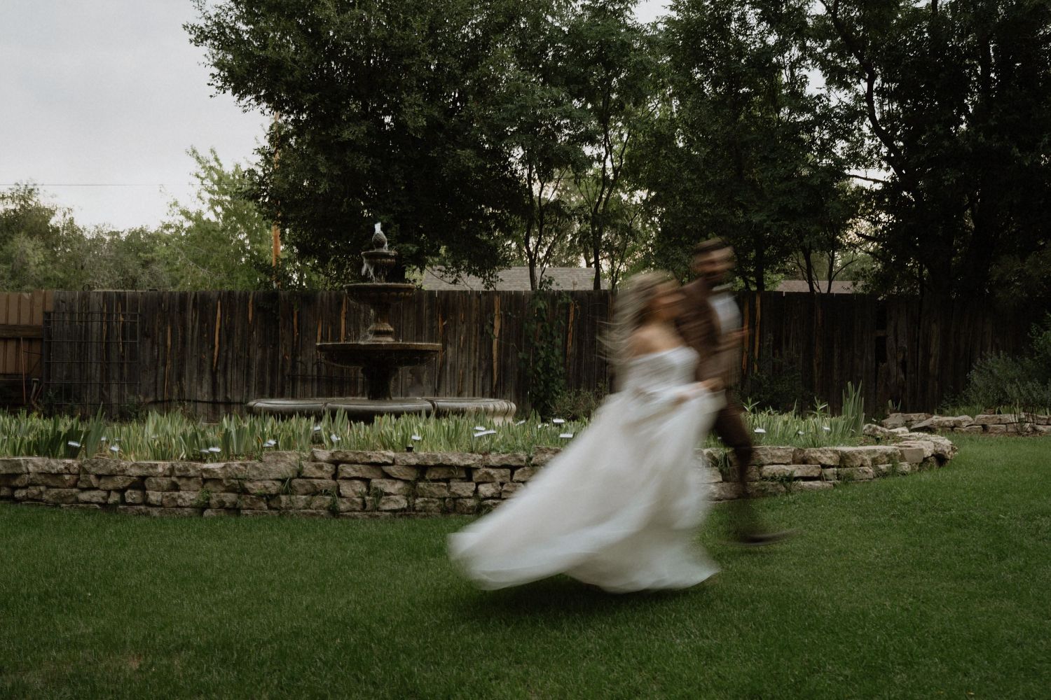 Blurred motion shot of a couple dancing in a lush backyard garden during an outdoor wedding celebration.
