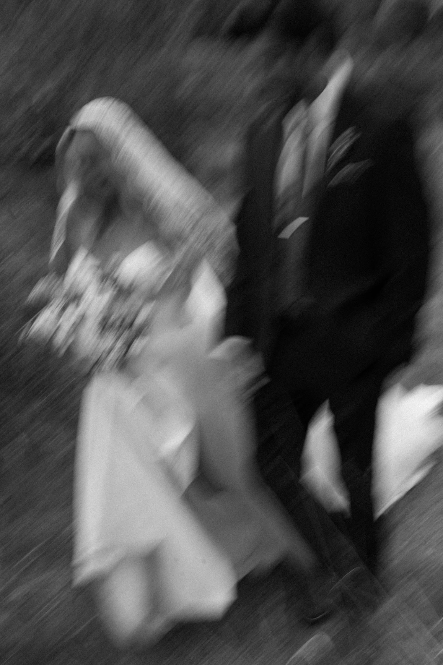 Blurred black and white photo of a bride and groom walking together, capturing motion and romance.