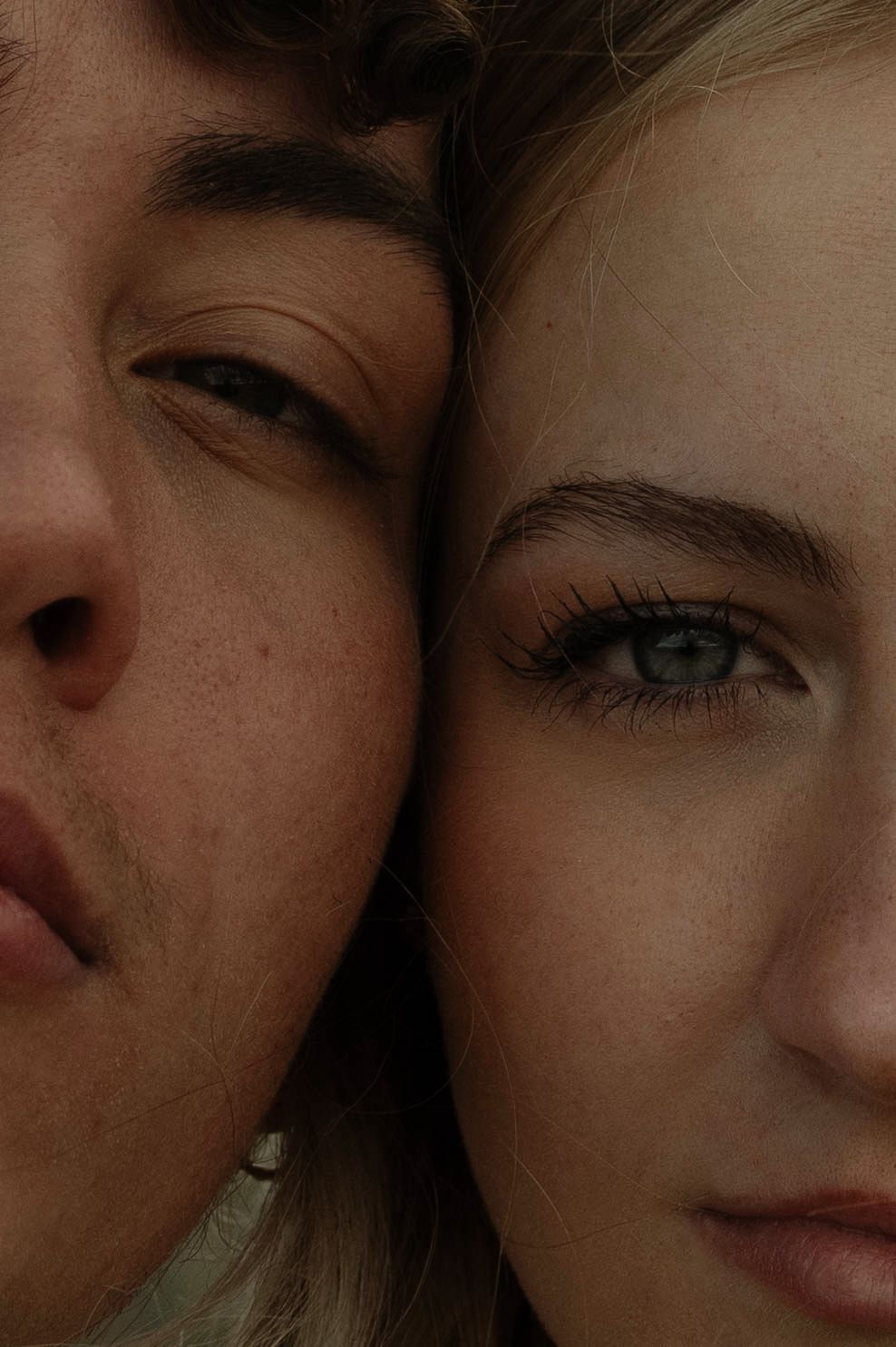 Close-up portrait of two young women with fair skin, cheeks touching, one winking and one with green eyes looking forward.