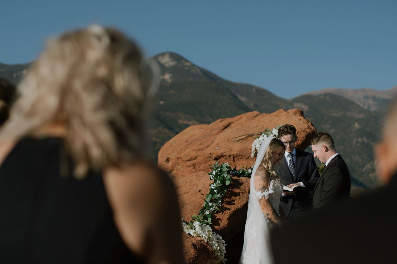 Bride and groom at outdoor wedding ceremony with stunning red rock formations and mountain backdrop.