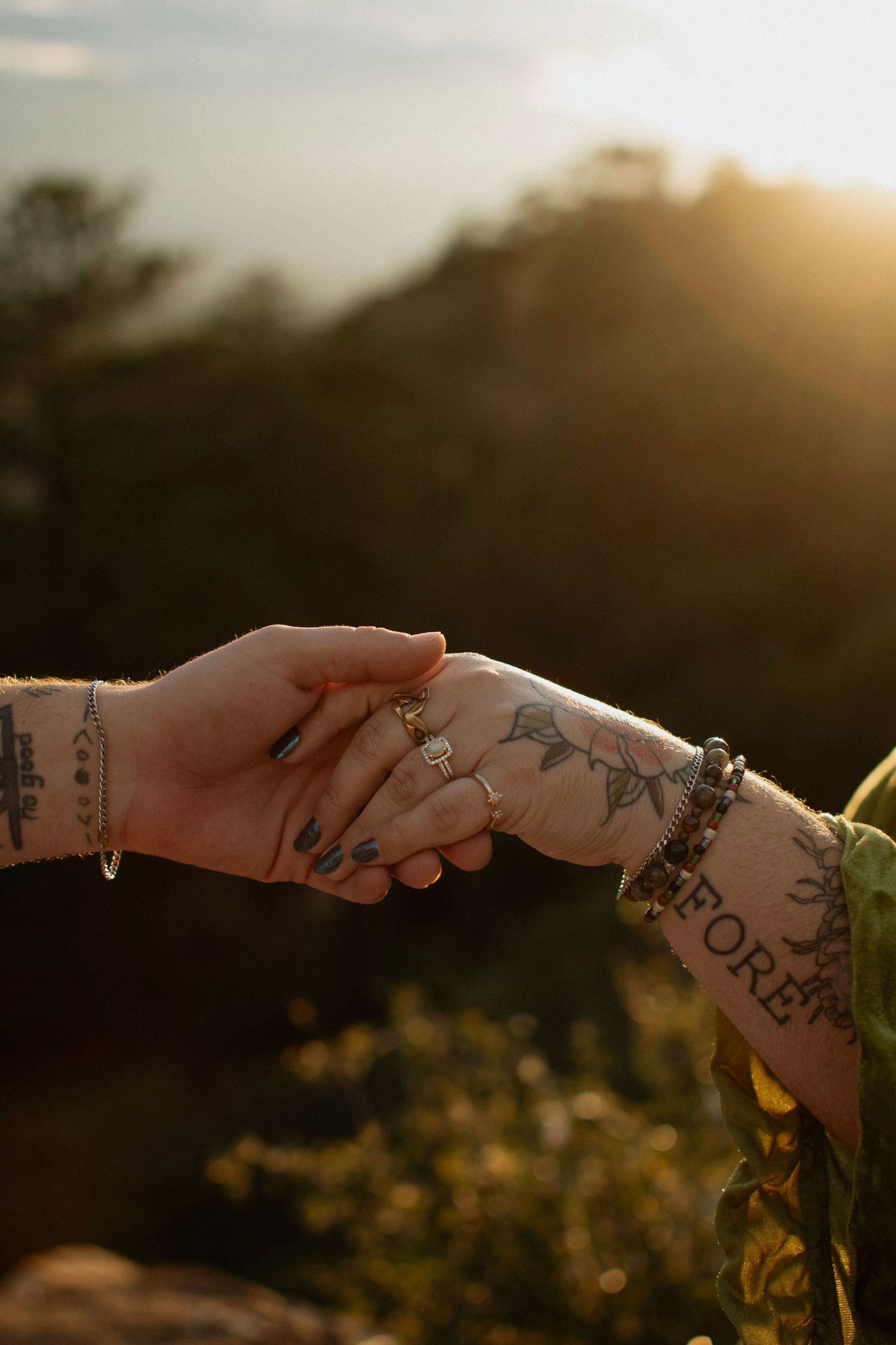 Close-up of tattooed hands holding engagement ring at golden sunset.
