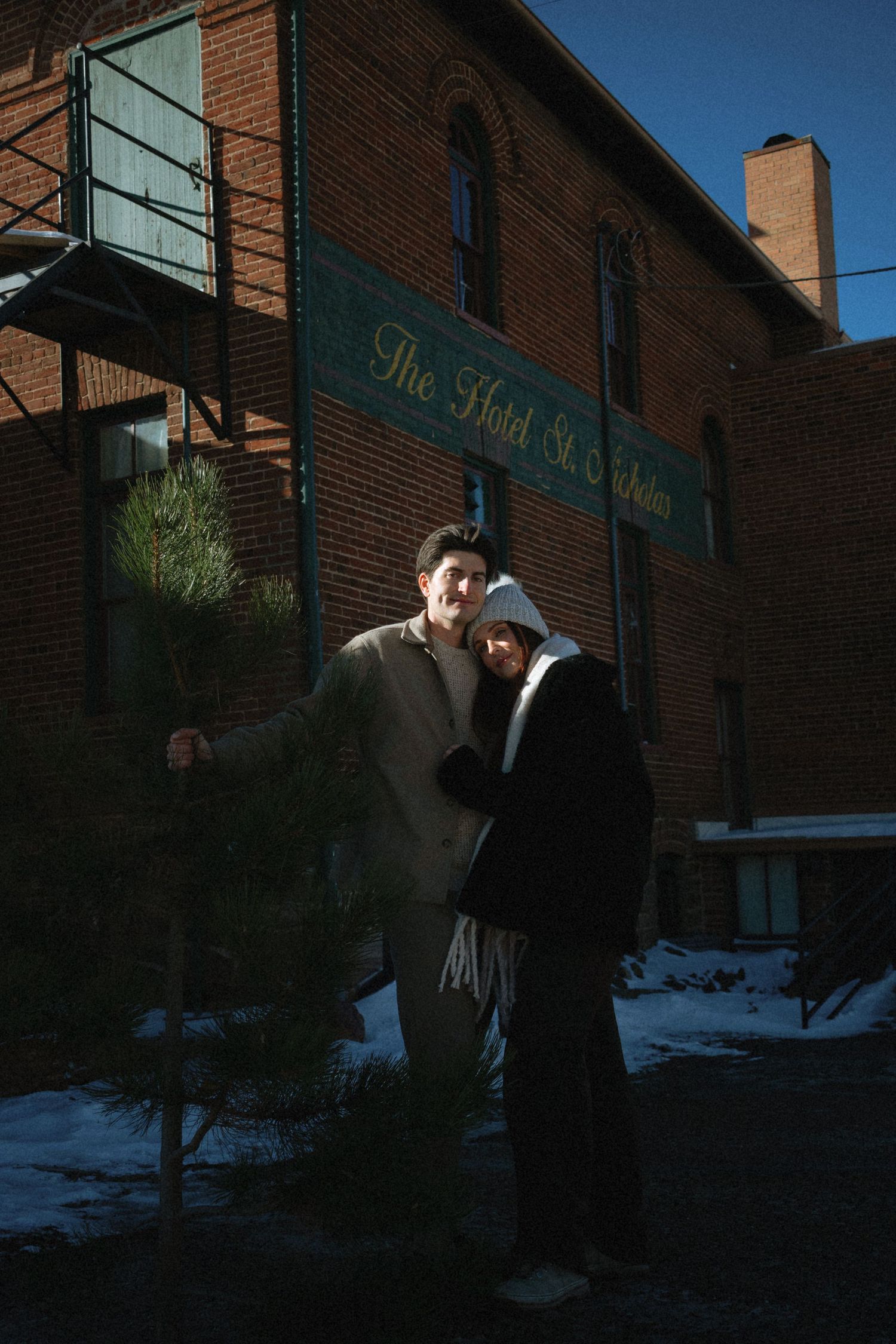 Smiling couple posing together outside The Hotel St. Charles in winter sunlight.