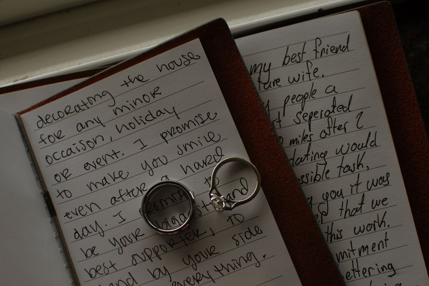 Wedding rings resting on handwritten love letter vows in open journal, romantic marriage proposal note closeup.