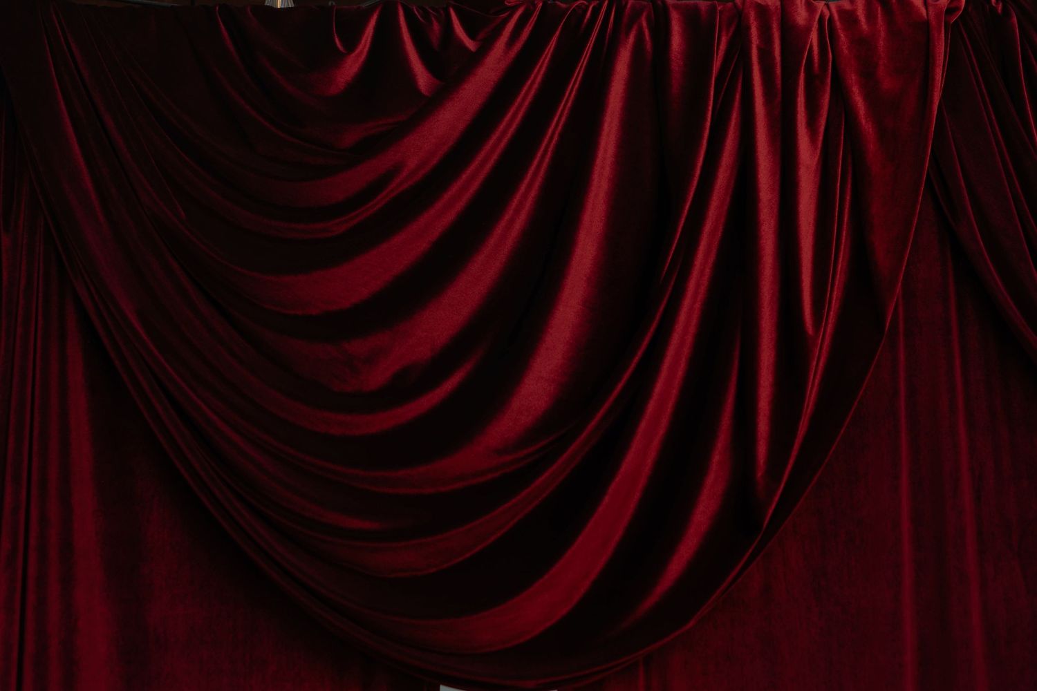 Luxurious deep red velvet theater curtains with elegant draped folds creating a dramatic stage backdrop.