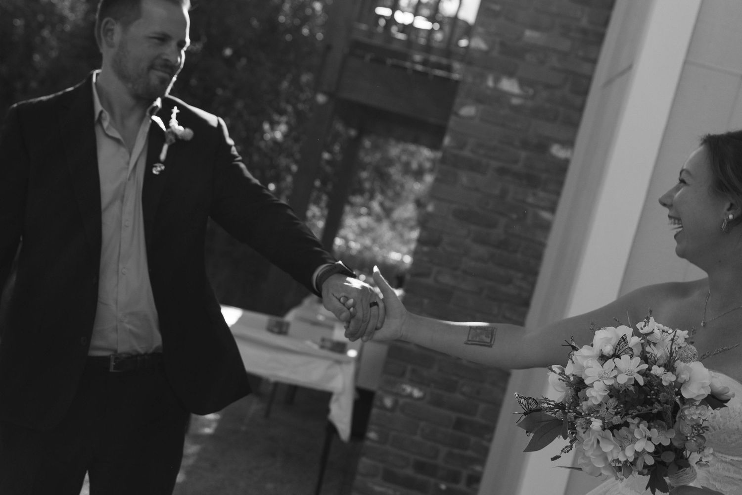 Black and white photo of a bride and groom holding hands at their outdoor wedding ceremony.