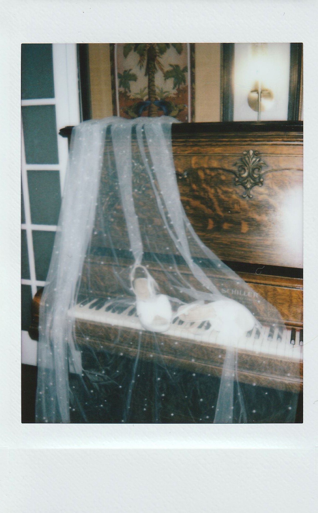A bridal veil draped over a vintage upright piano with white wedding shoes resting on the keys.