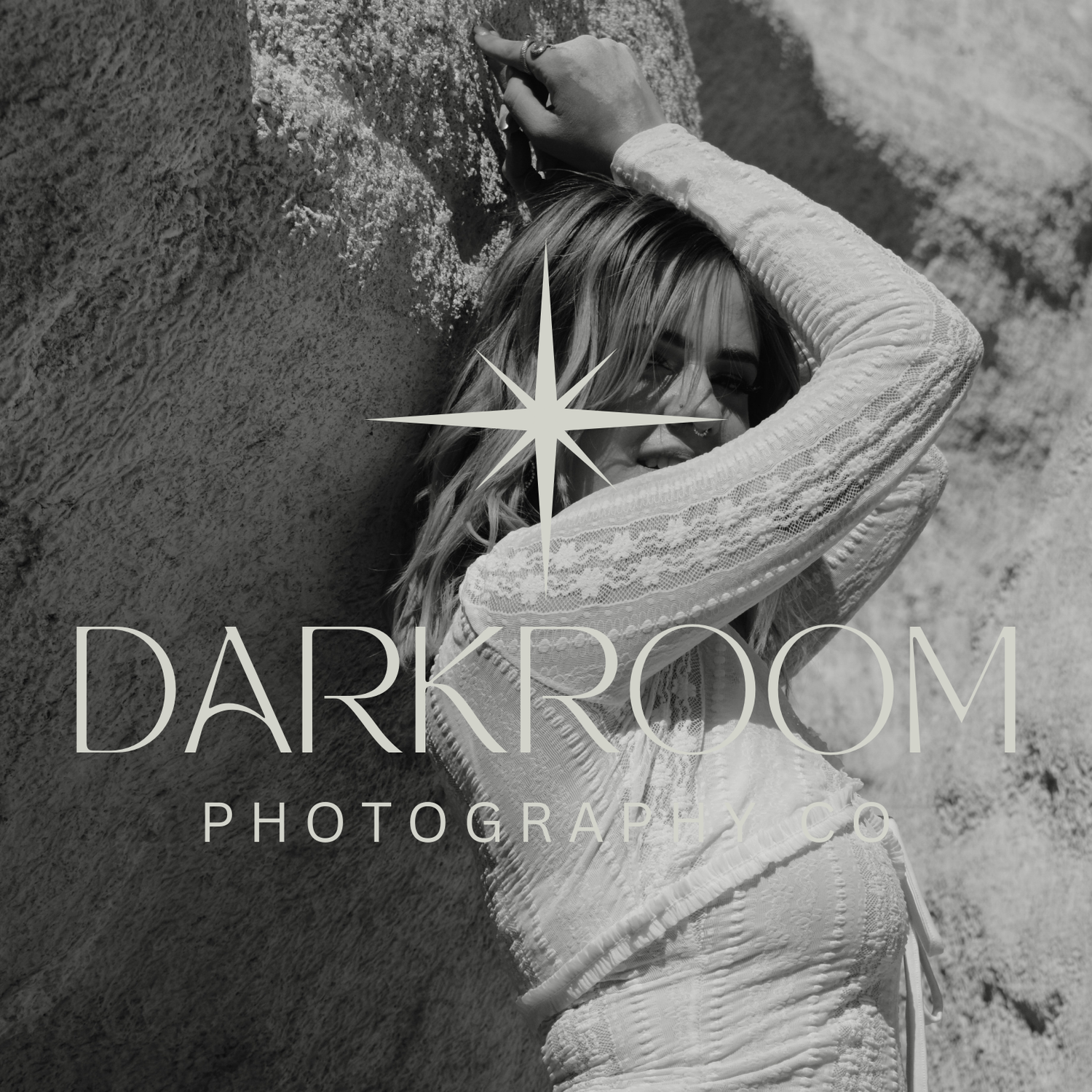 Black and white portrait of woman leaning against rock wall, Darkroom Photography logo overlay.