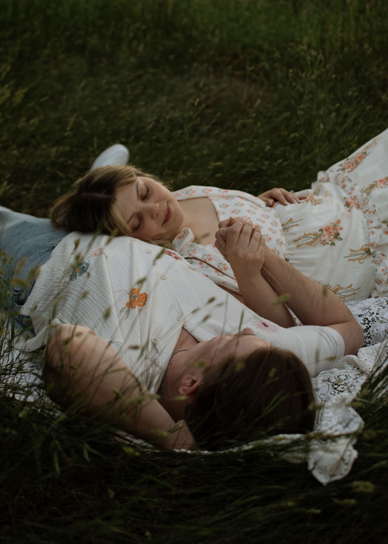 Romantic couple lying together in lush green grass holding hands.