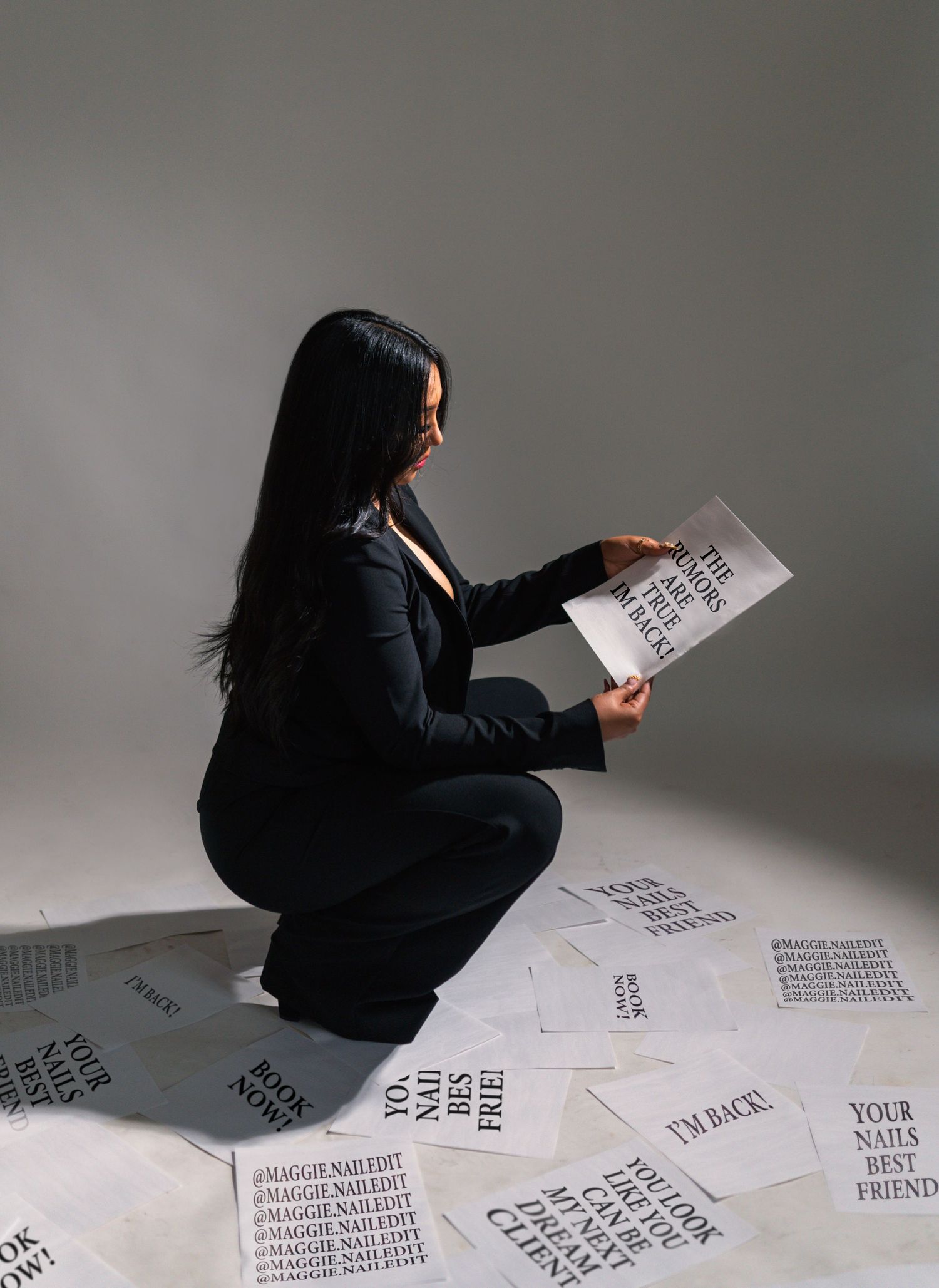 A person in black clothing arranges paper documents across a gray floor in an artistic composition.