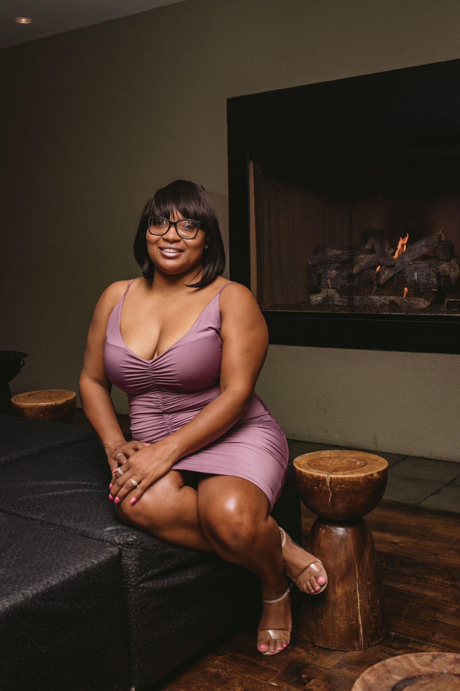 A person wearing a purple dress poses indoors on a wooden stool during a portrait photography session.