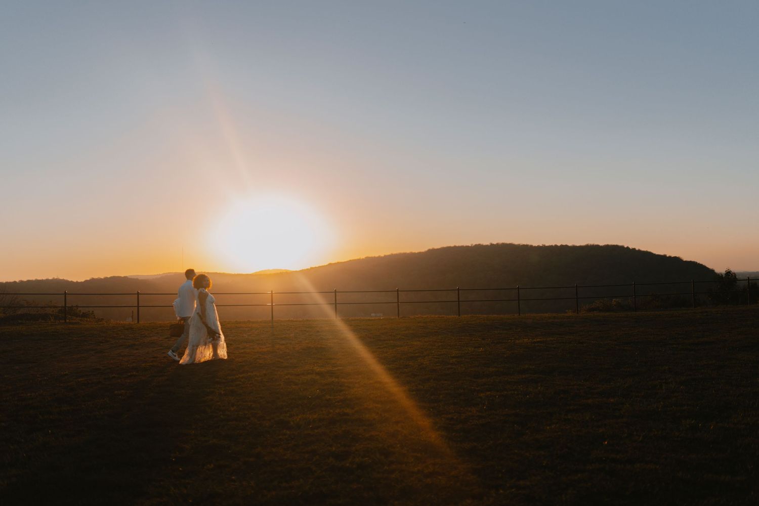 Sun setting over rolling hills casting golden light across a rural landscape at dusk.