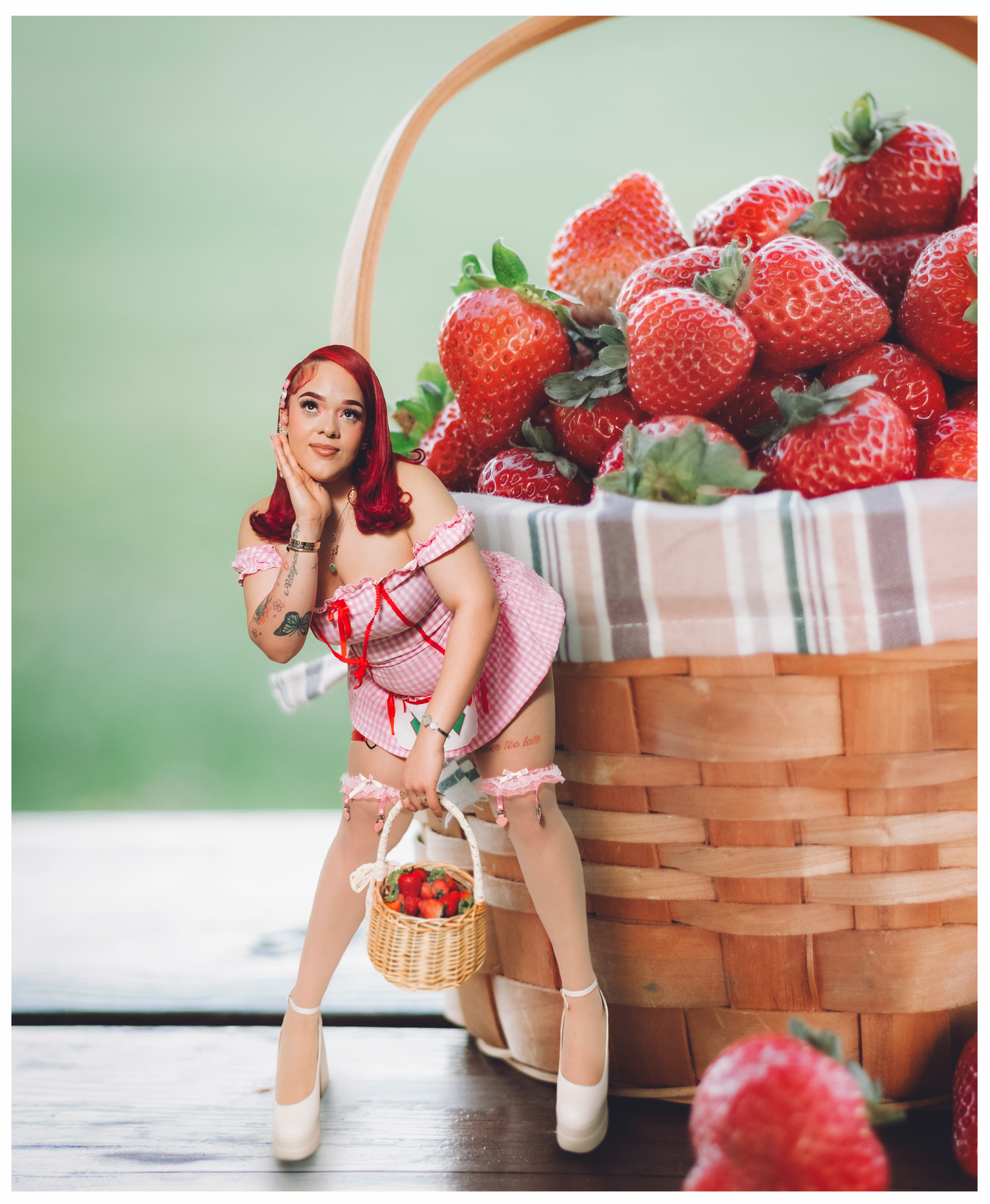 Whimsical portrait of a woman in pink dress next to giant strawberry basket.