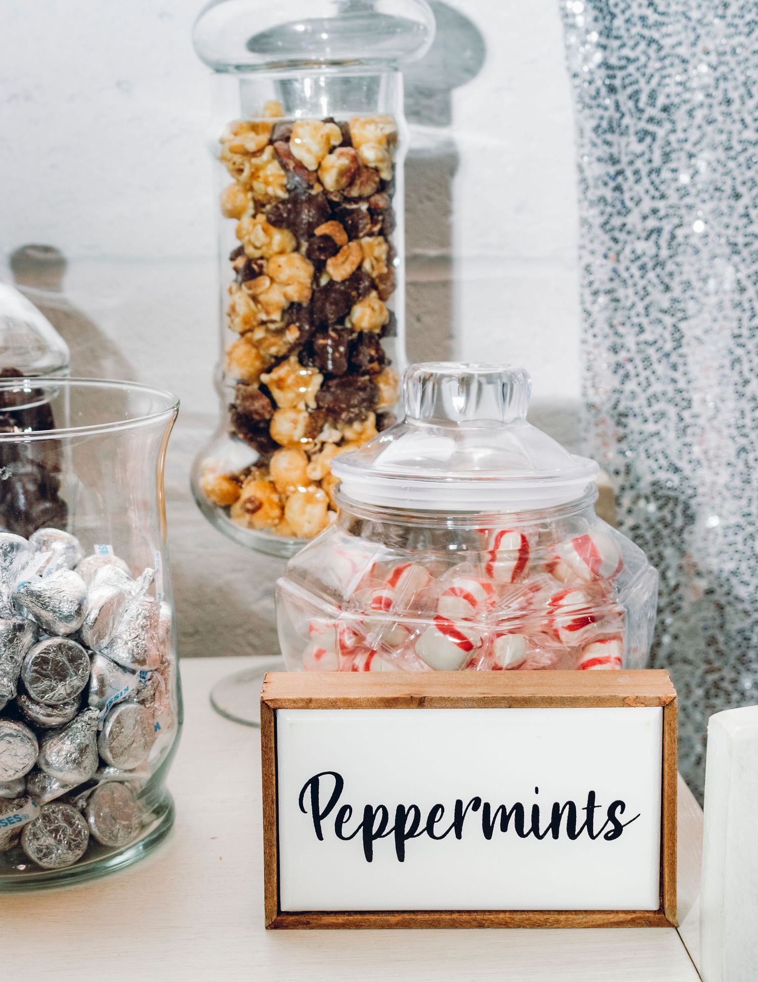 Glass apothecary jars with rustic labels filled with candy and treats displayed on a white counter.