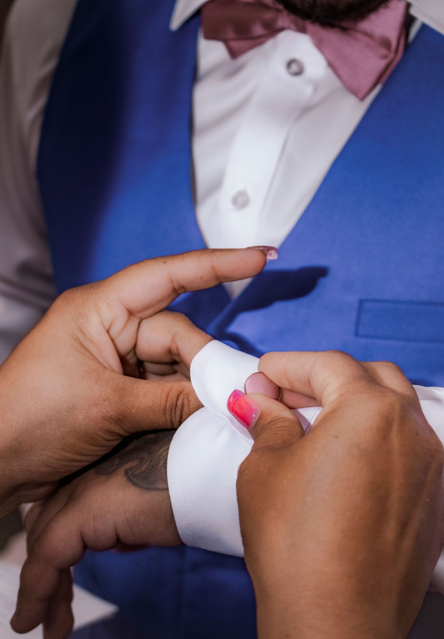 Close up of hands adjusting white dress shirt buttons and pink bowtie.