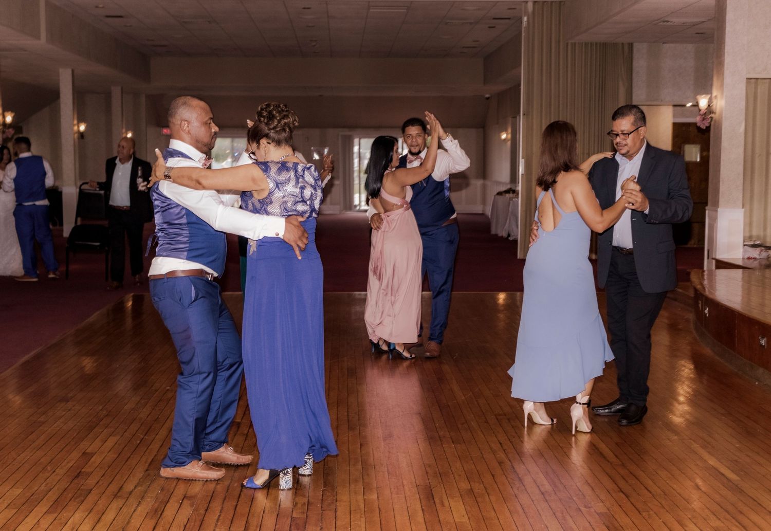 Couples dancing together on a wooden floor at an indoor event.
