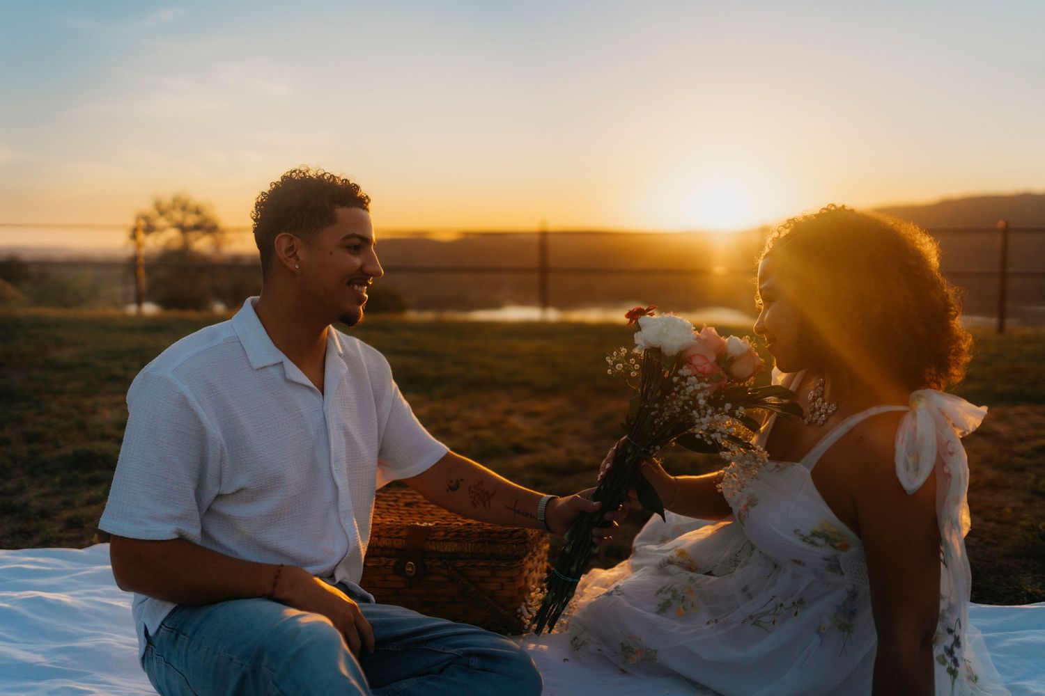 A romantic couple embraces during golden hour sunset in a scenic outdoor setting with warm glowing sunlight.