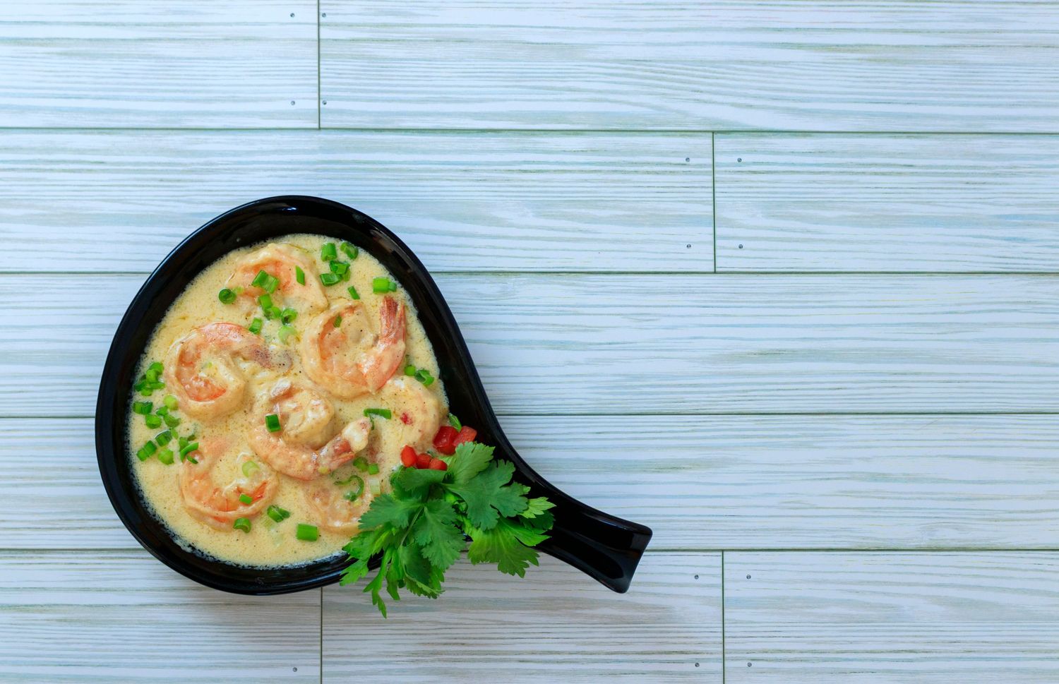 Creamy shrimp curry sauce in a black pan with fresh herbs on wooden surface.