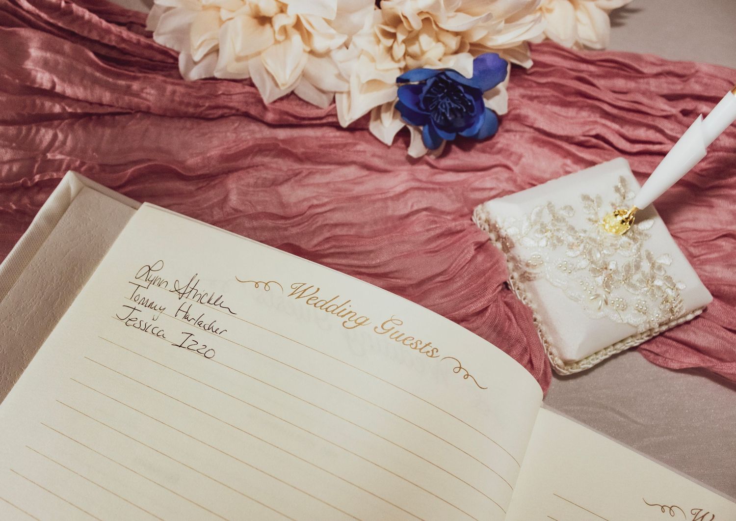 Open journal with pen and flowers on pink silk fabric.