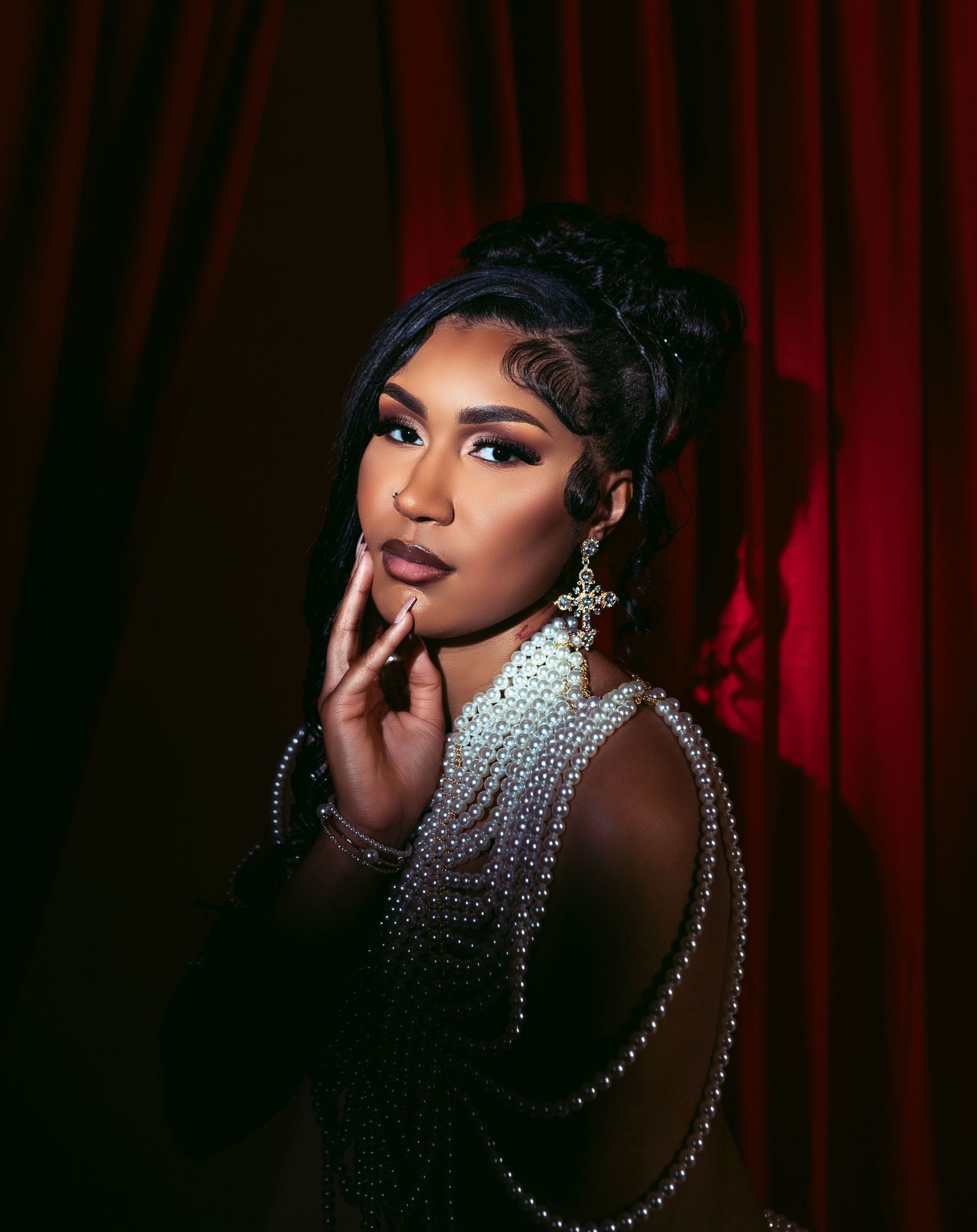 Dramatic portrait with crystal jewelry against red curtain backdrop.