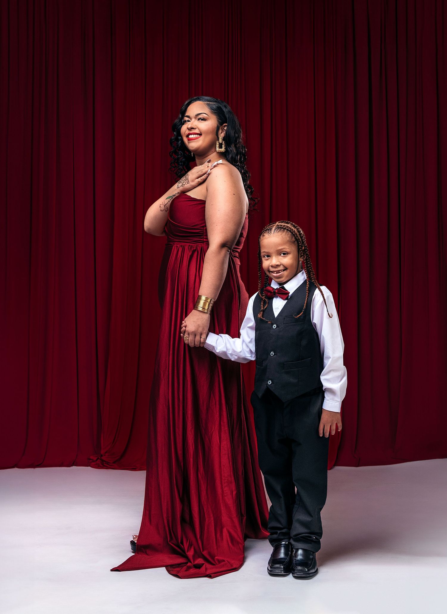 An elegant pair in formal attire pose against a red curtain backdrop for a special occasion portrait.