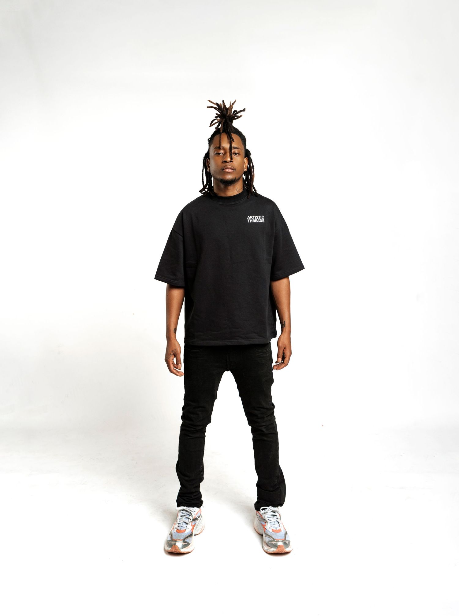 Person in black t-shirt and dark jeans poses in streetwear style against white background.