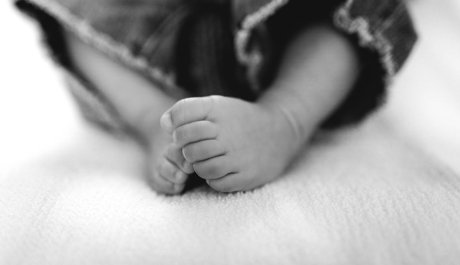 Black and white close-up photo of a newborn baby's tiny feet resting on a soft white blanket.