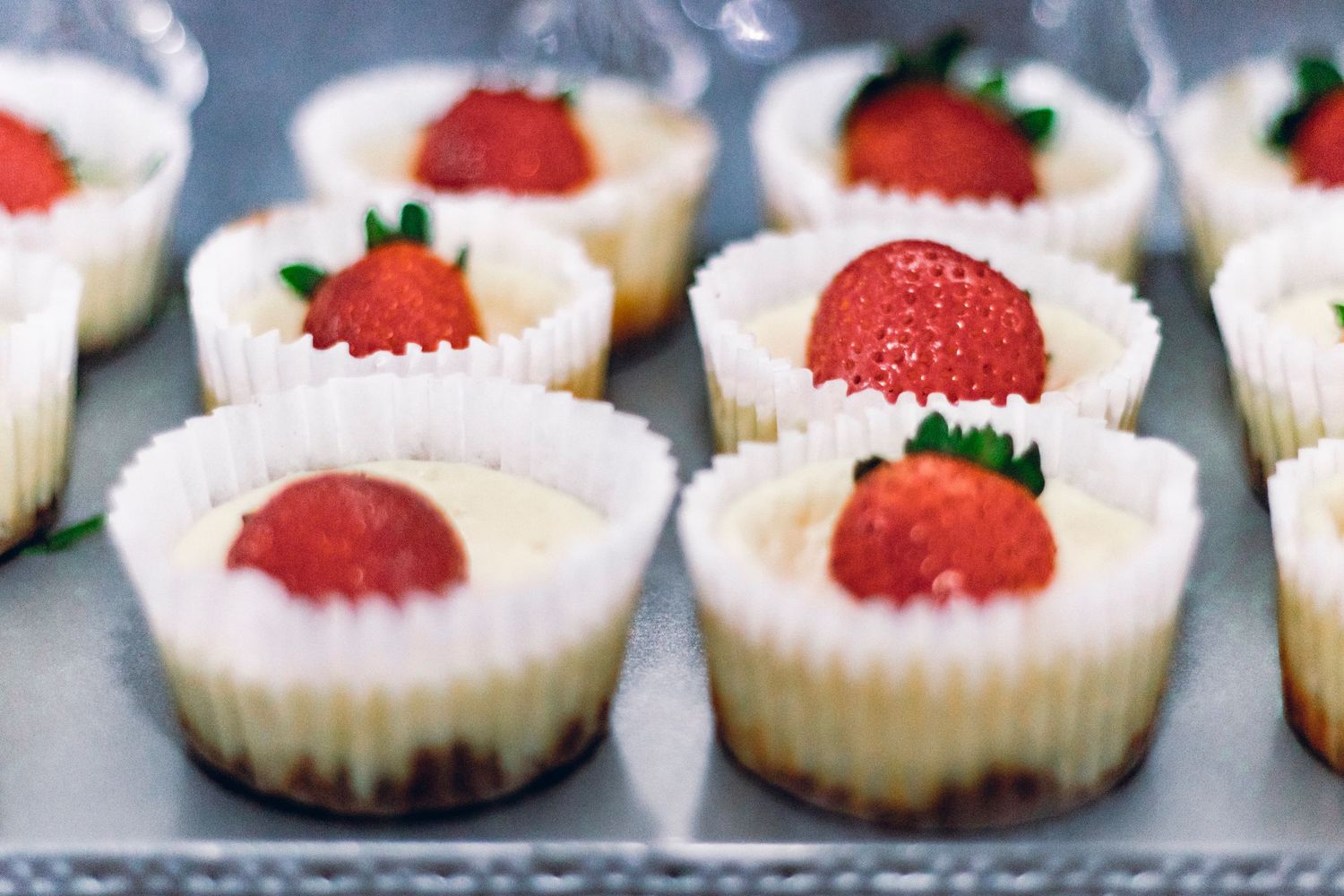 Mini strawberry cheesecake bites arranged in white paper liners on a metal tray.