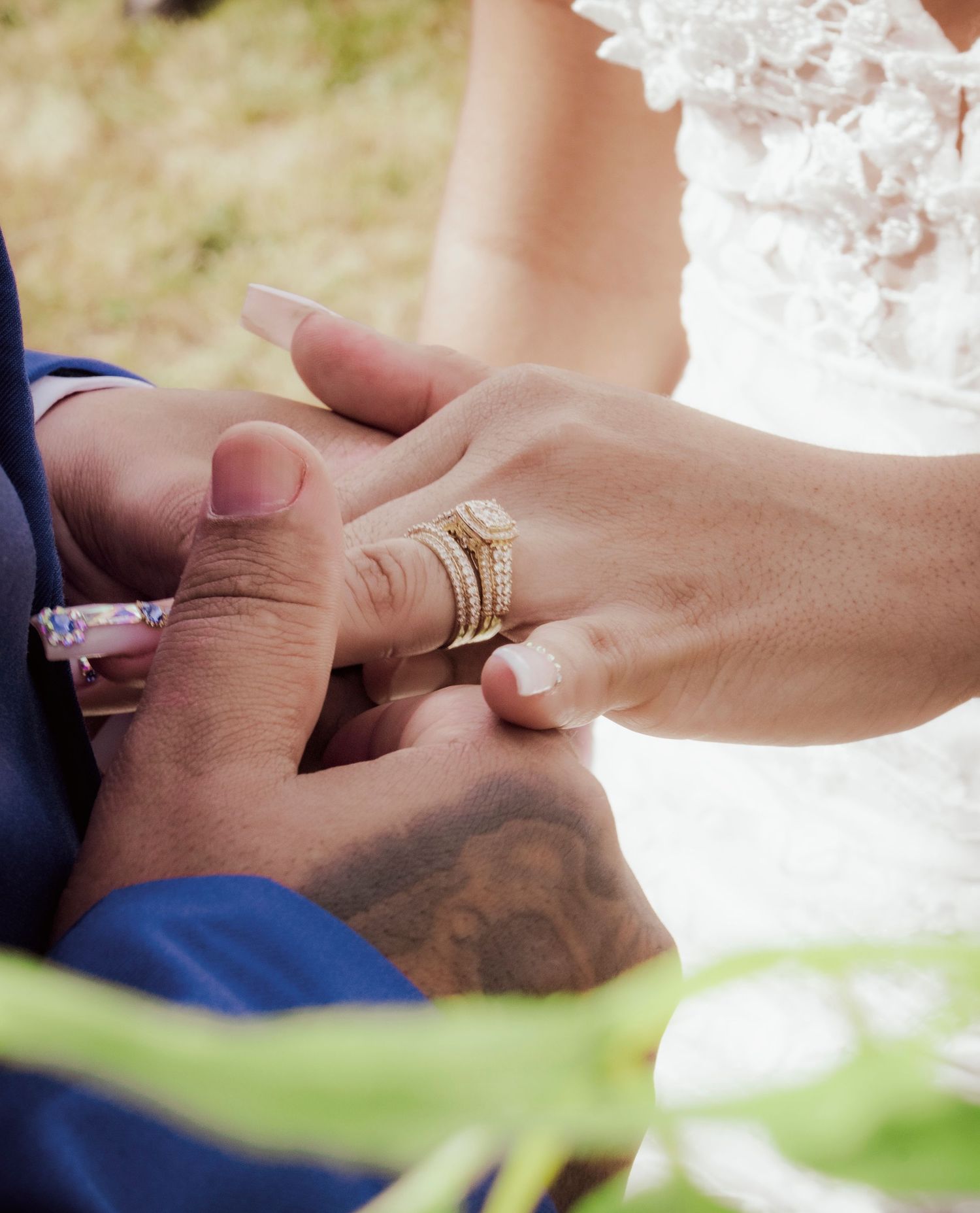 Close-up of wedding rings being exchanged during ceremony with blue suit and white dress visible.