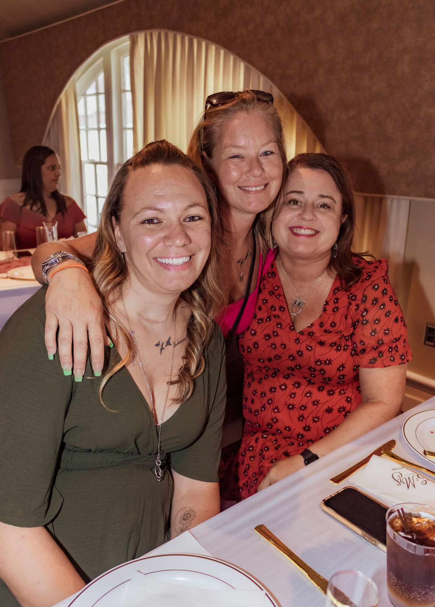Three friends sharing a joyful moment together at a restaurant gathering.