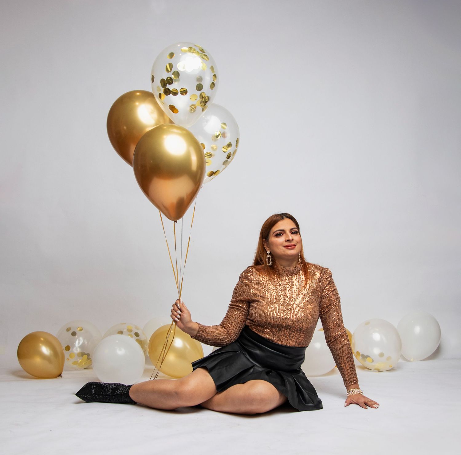 A festive studio portrait with gold and clear balloons against a light grey background.