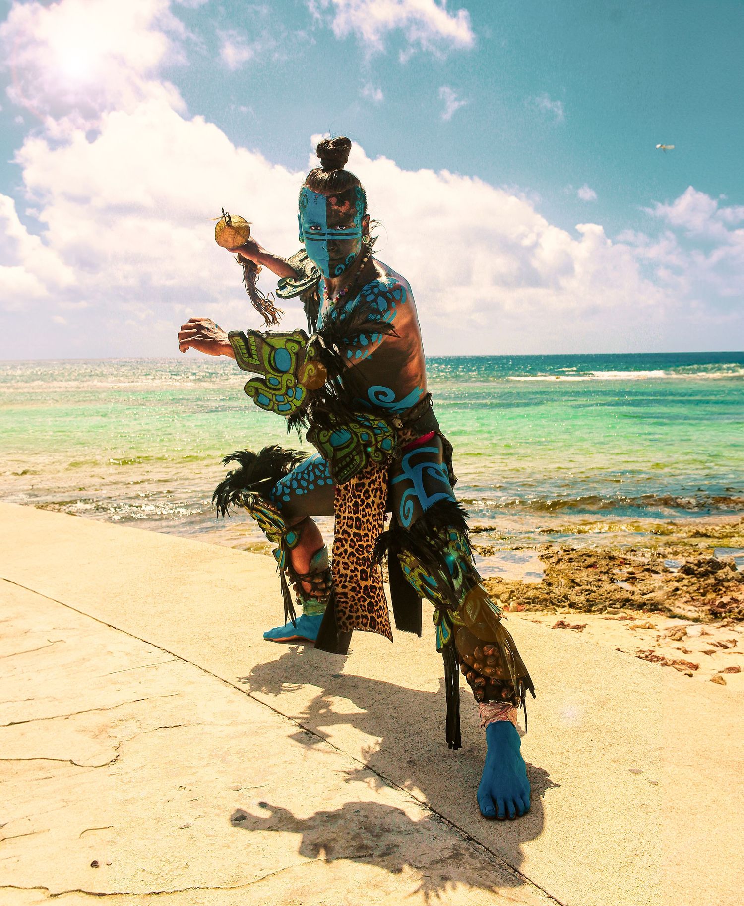 Colorful traditional dancer performs on beach wearing elaborate costume with turquoise and animal print details.