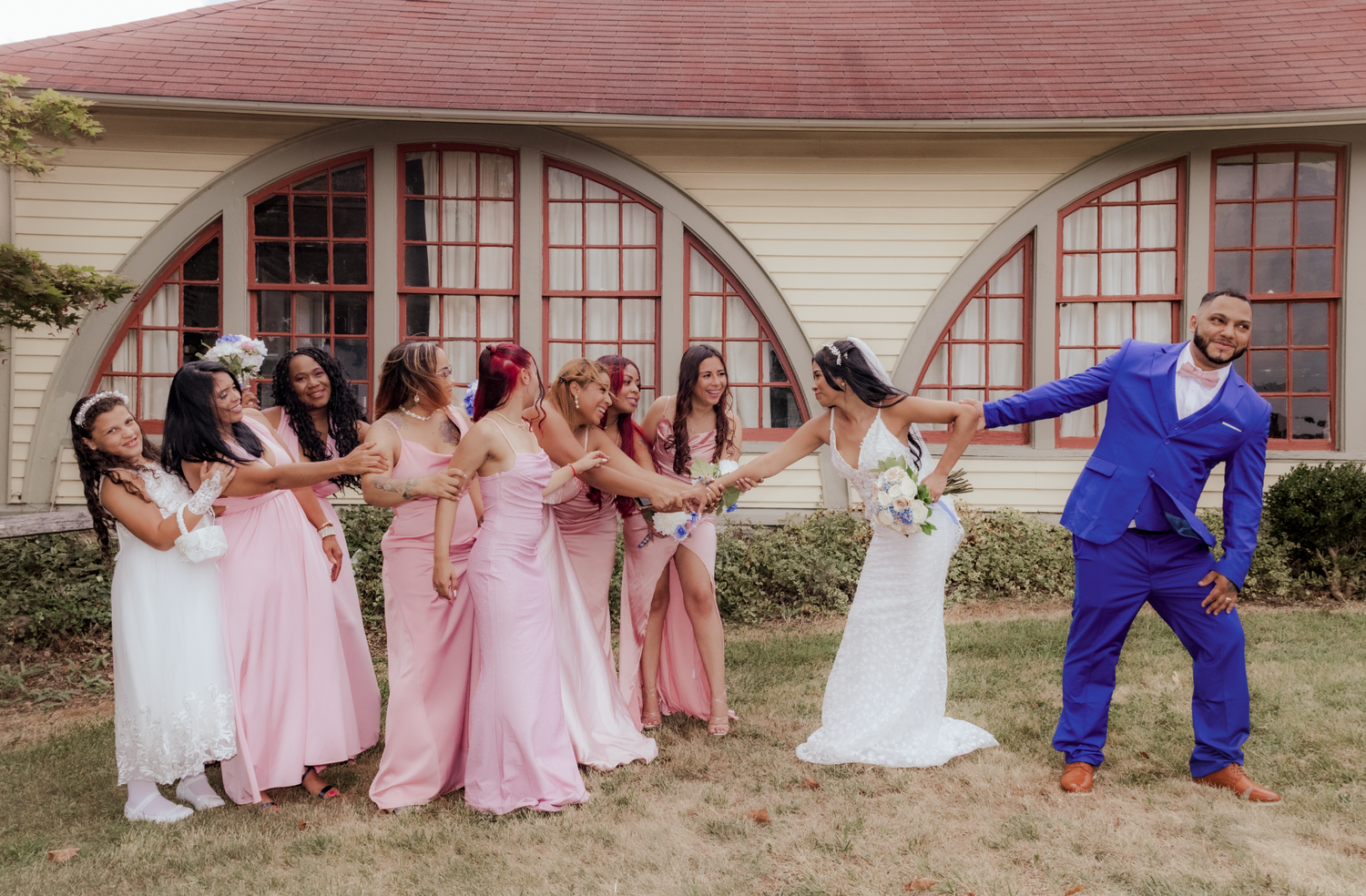 Wedding party poses for fun photo with bridesmaids in pink dresses and groom in blue suit.