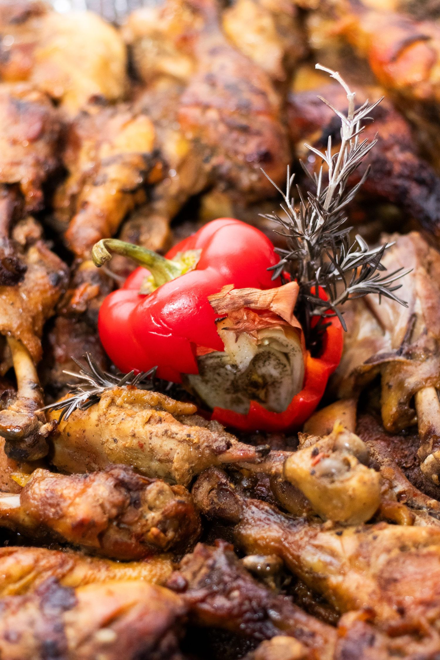 Grilled red bell pepper and rosemary garnish on a bed of roasted meat with charred edges.