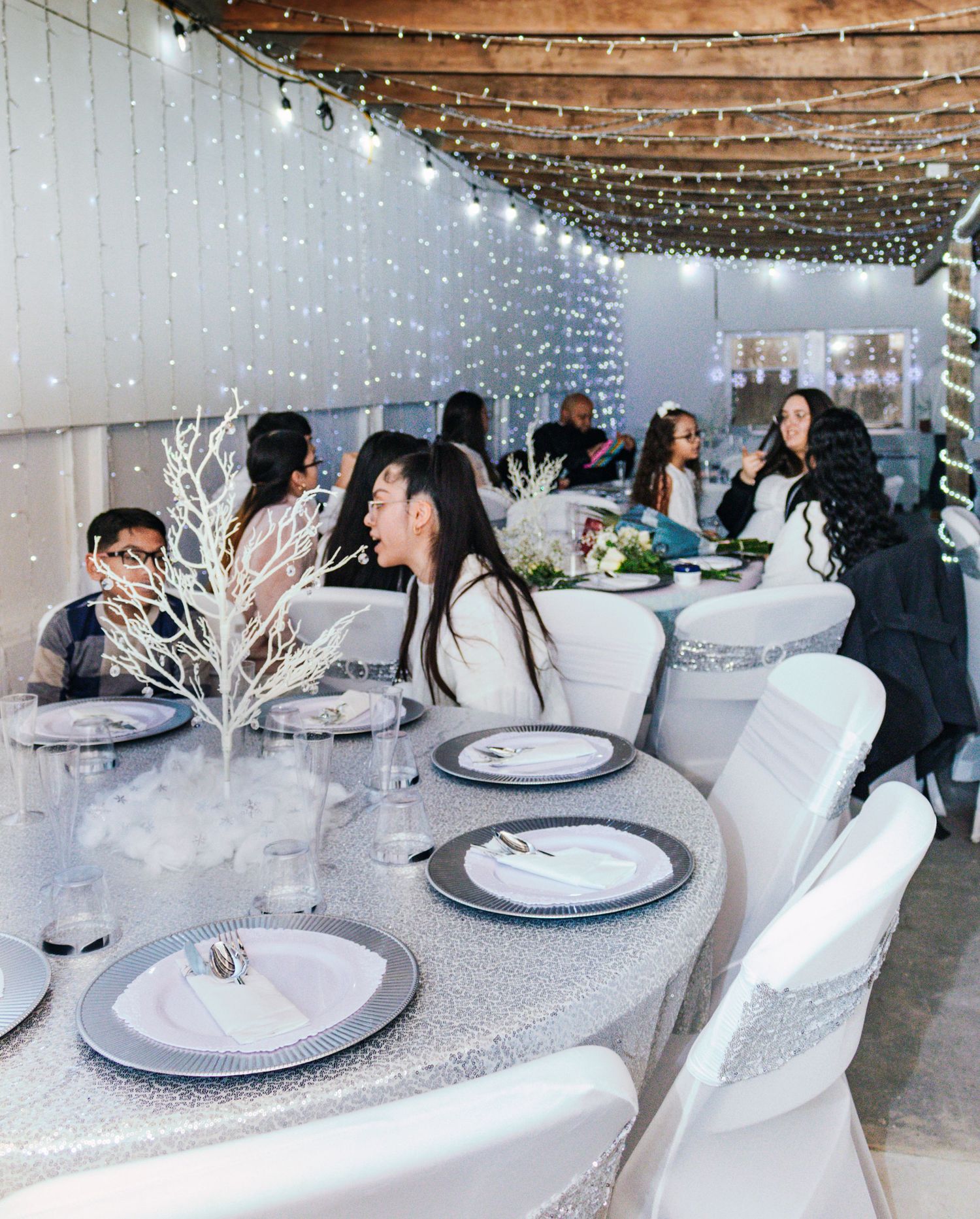 Elegant winter-themed indoor venue with white decor, twinkling lights, and dining tables set for a formal event.