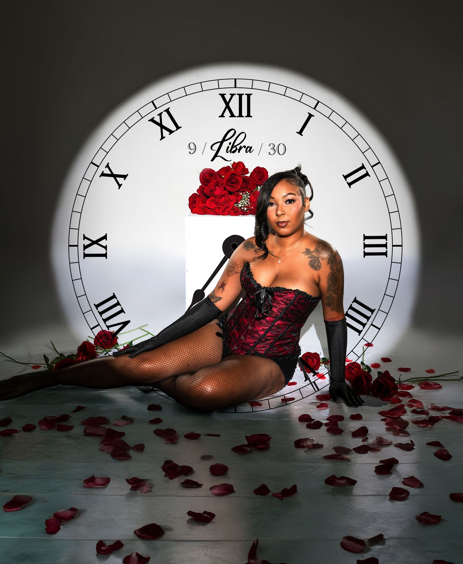Artistic boudoir photo with large clock face backdrop, red roses and scattered petals in moody lighting.