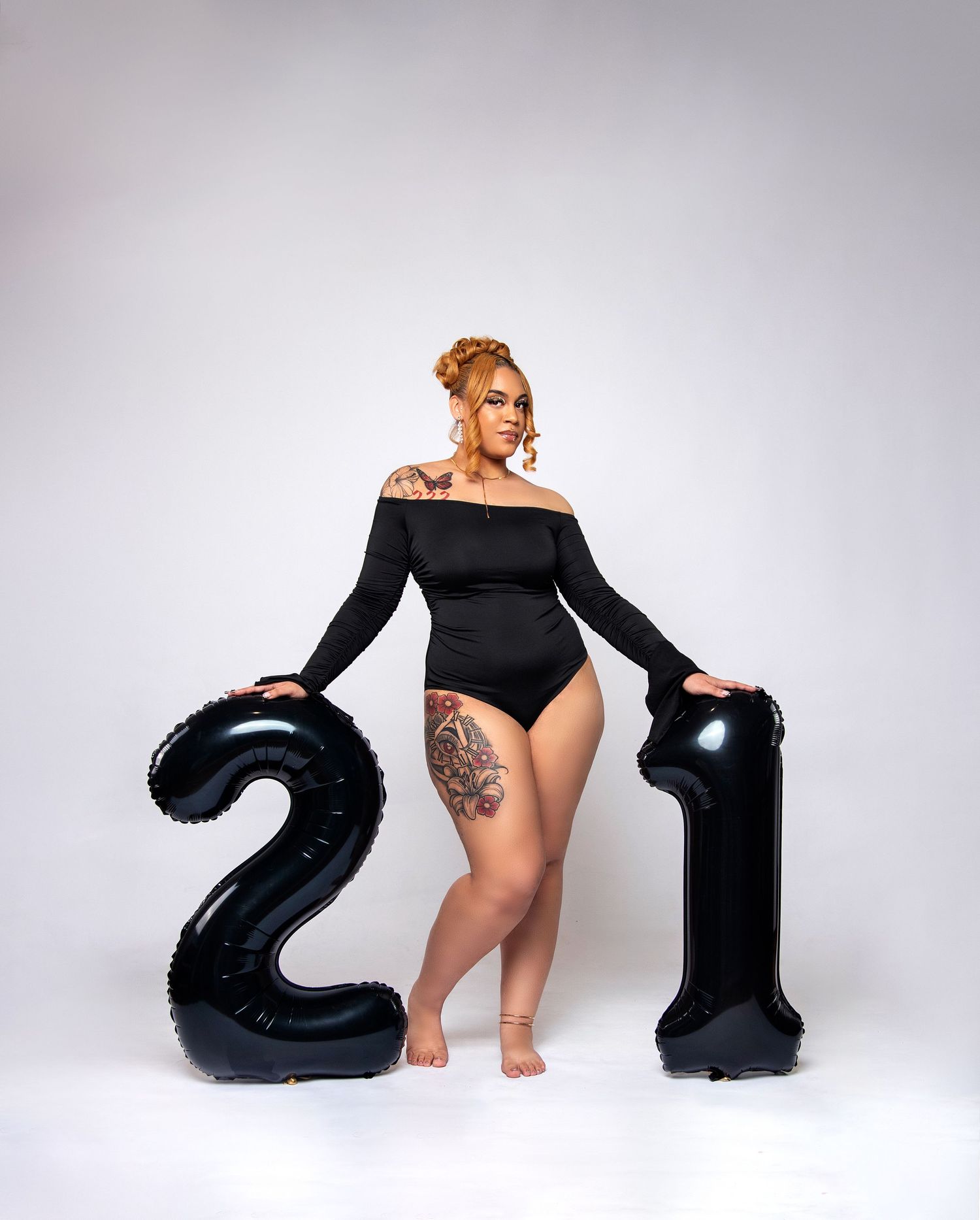 A stylish portrait with large black number 21 balloons against a white studio background.